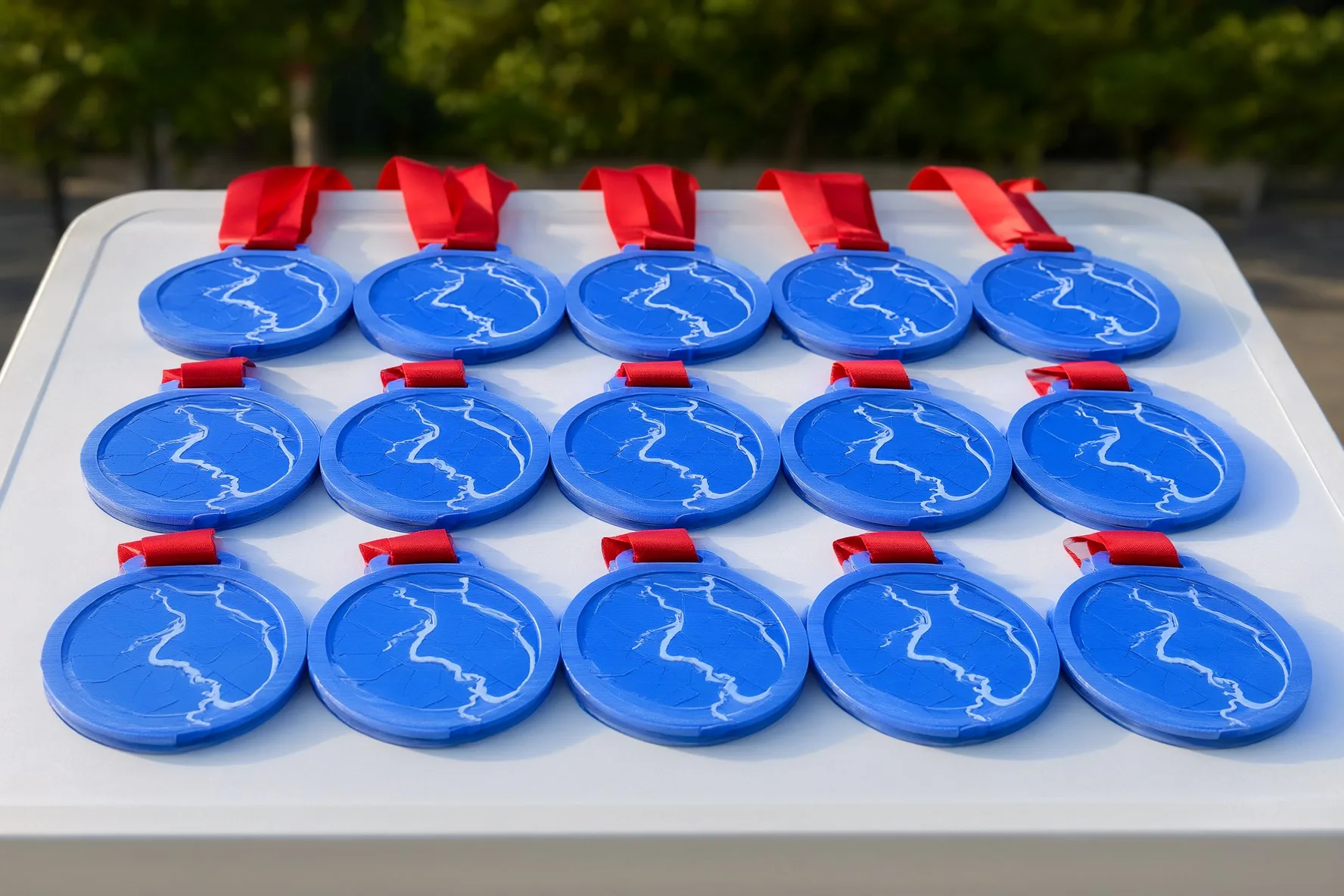 Rows of blue 3D printed medals with a white route line and red ribbons on a table at a race finish area